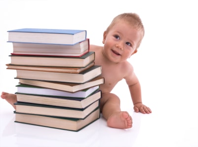 Baby boy smiling and sitting with a stack of books in front of him