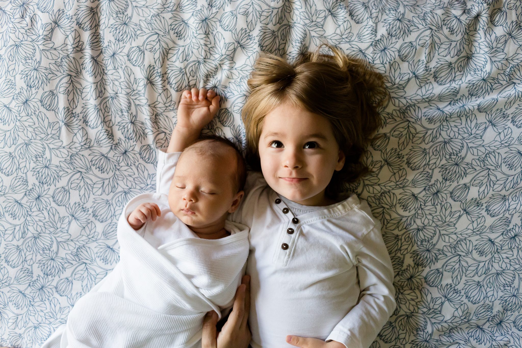 newborn with sibling lying on bed